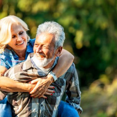 Portrait of American senior beautiful and happy mature couple around 70 years old showing love and affection smiling together in the park having a romantic walk husband carrying wife on his back.